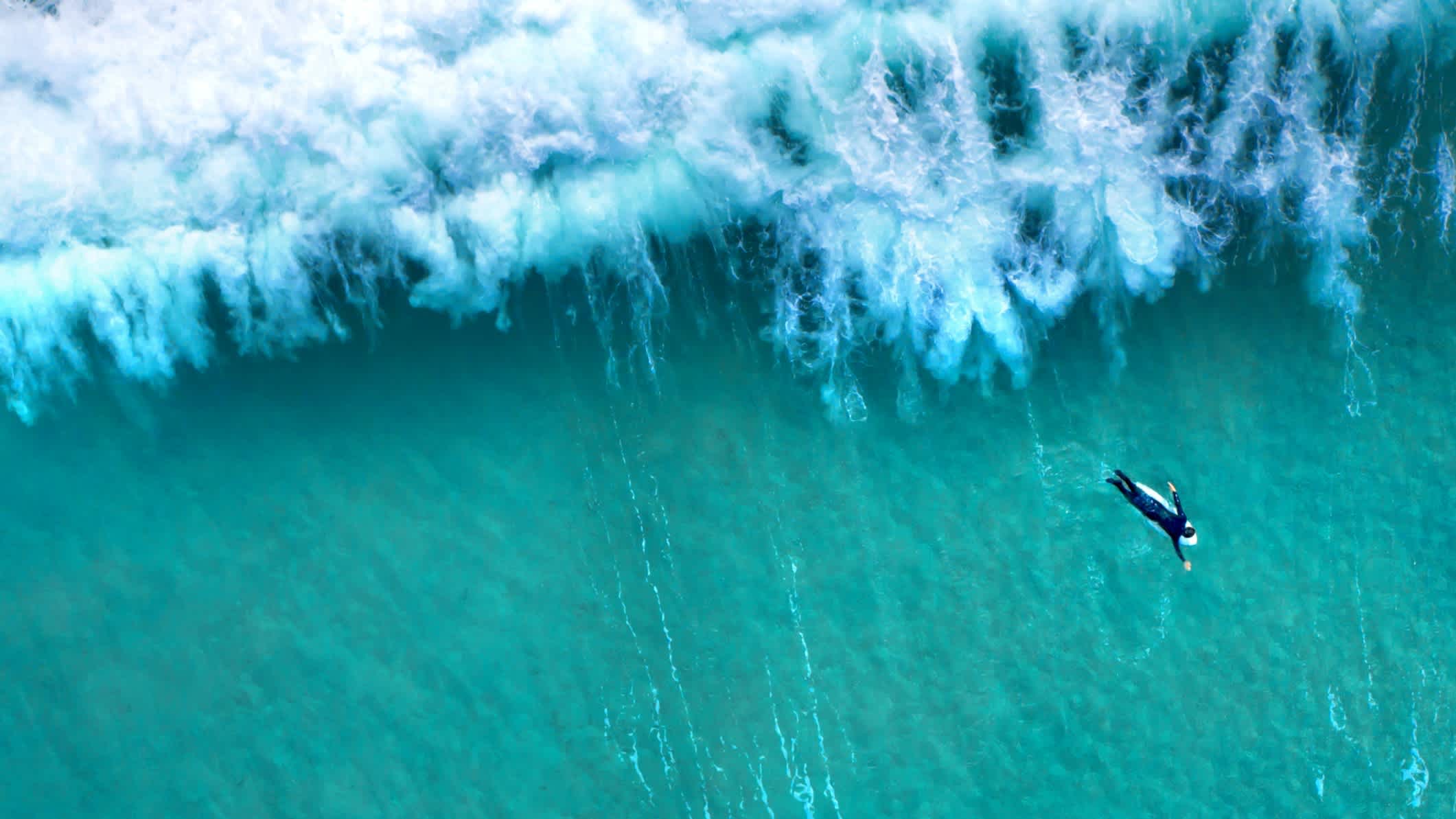 Große Welle plätschert hinter einem einsamen Surfer von oben gesehen