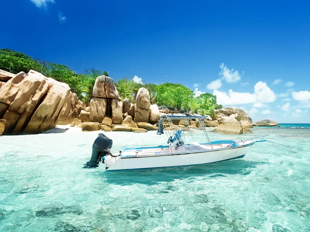 Motorboot im kristallklaren Wasser vor Granitfelsen und tropischer Vegetation. Seychellen.