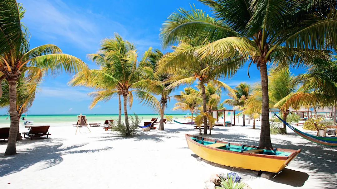 Strand mit Palmen, Hängematten und einem Holzboot auf weißem Sand. Holbox, Quintana Roo, Mexiko.