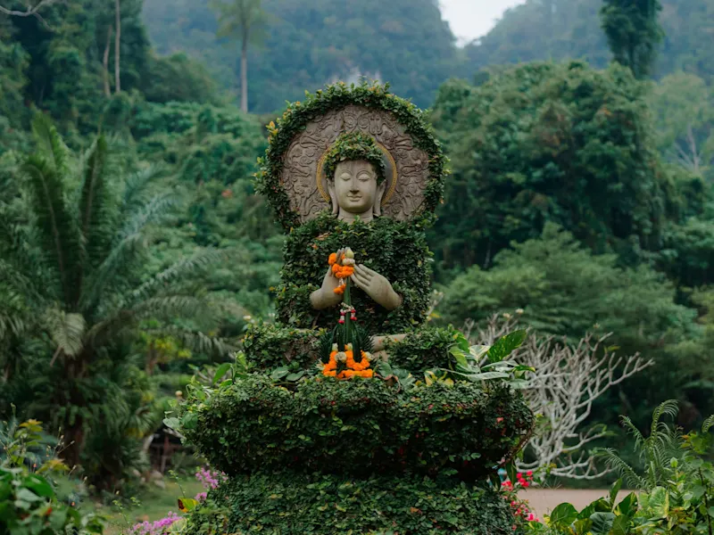 Krabi, Thailand Mit Pflanzen bewachsene Buddha-Statue inmitten tropischer Vegetation, Krabi, Thailand.