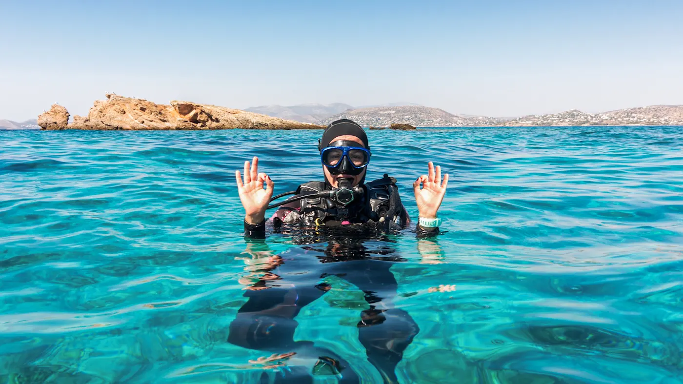 Une plongeuse en combinaison noire montre le signe OK dans l'eau turquoise. Oman.