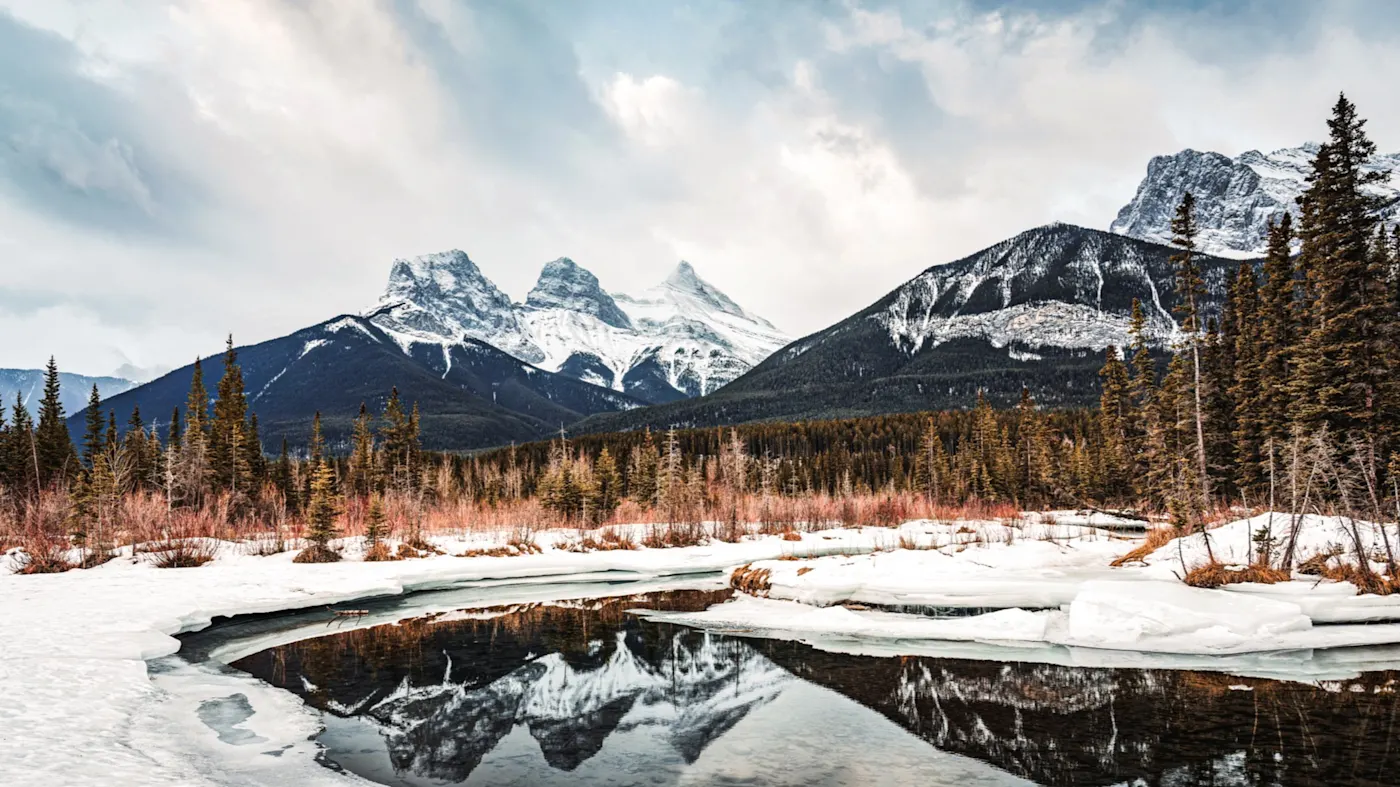 Canmore, Alberta, Kanada Die Three Sisters-Gipfel spiegeln sich in einem gefrorenen See mit schneebedeckter Landschaft. Canmore, Alberta, Kanada.