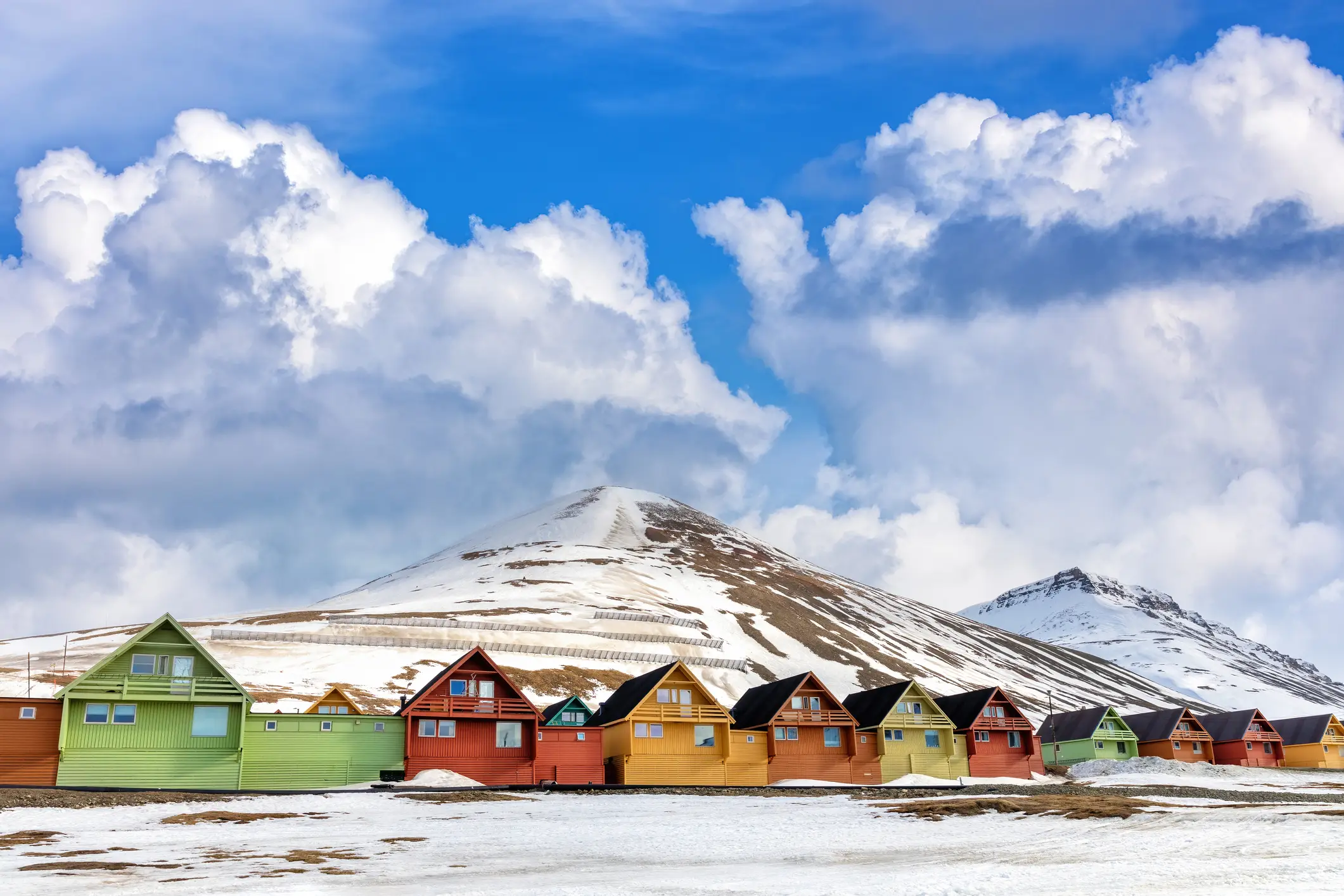 Bunte, in einer Reihe stehende Häuser Holzhäuser vor einem verschneiten Berg