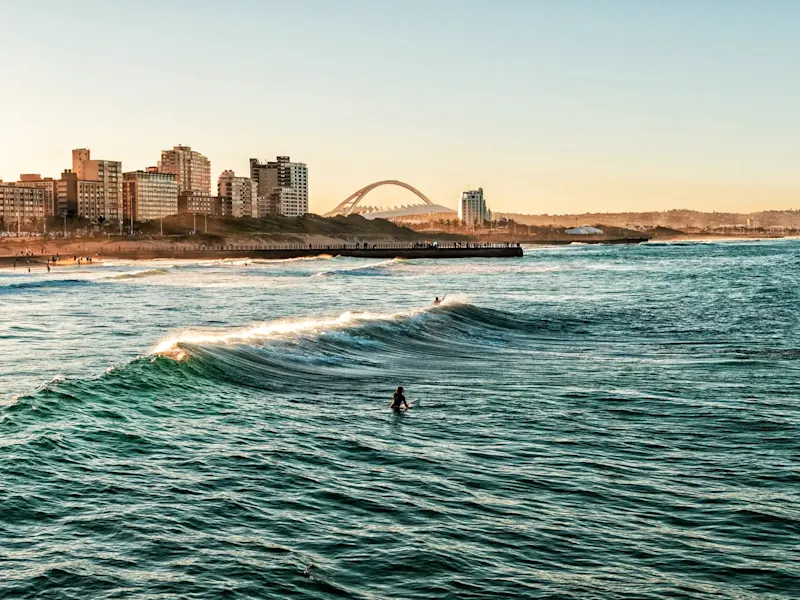 Südafrika, Durban Wellen brechen am Sandstrand mit Skyline und Brücke im Hintergrund. Durban, Südafrika.