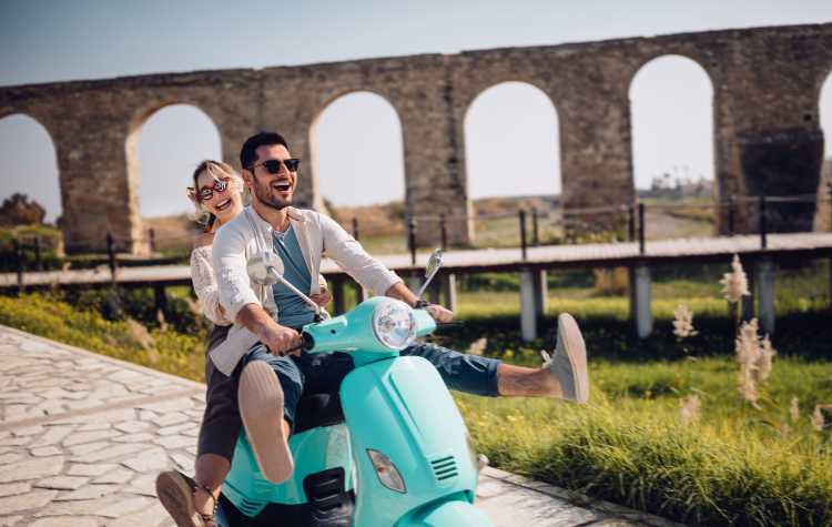 Glückliches junges paar Reiten Retro-Scooter in mediterranen Altstadt

