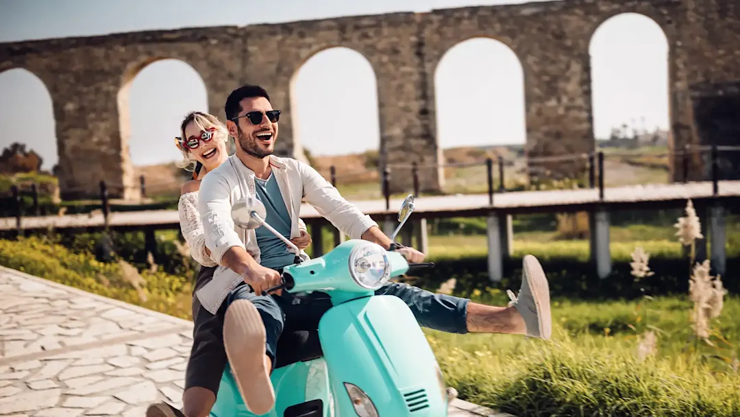 Glückliches junges paar Reiten Retro-Scooter in mediterranen Altstadt

