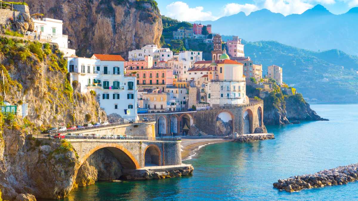 Europe, Italie, Côte Amalfitaine, maisons colorées à flanc de falaise surplombant une baie bleue. Silhouettes de montagnes et ciel bleu en arrière-plan.