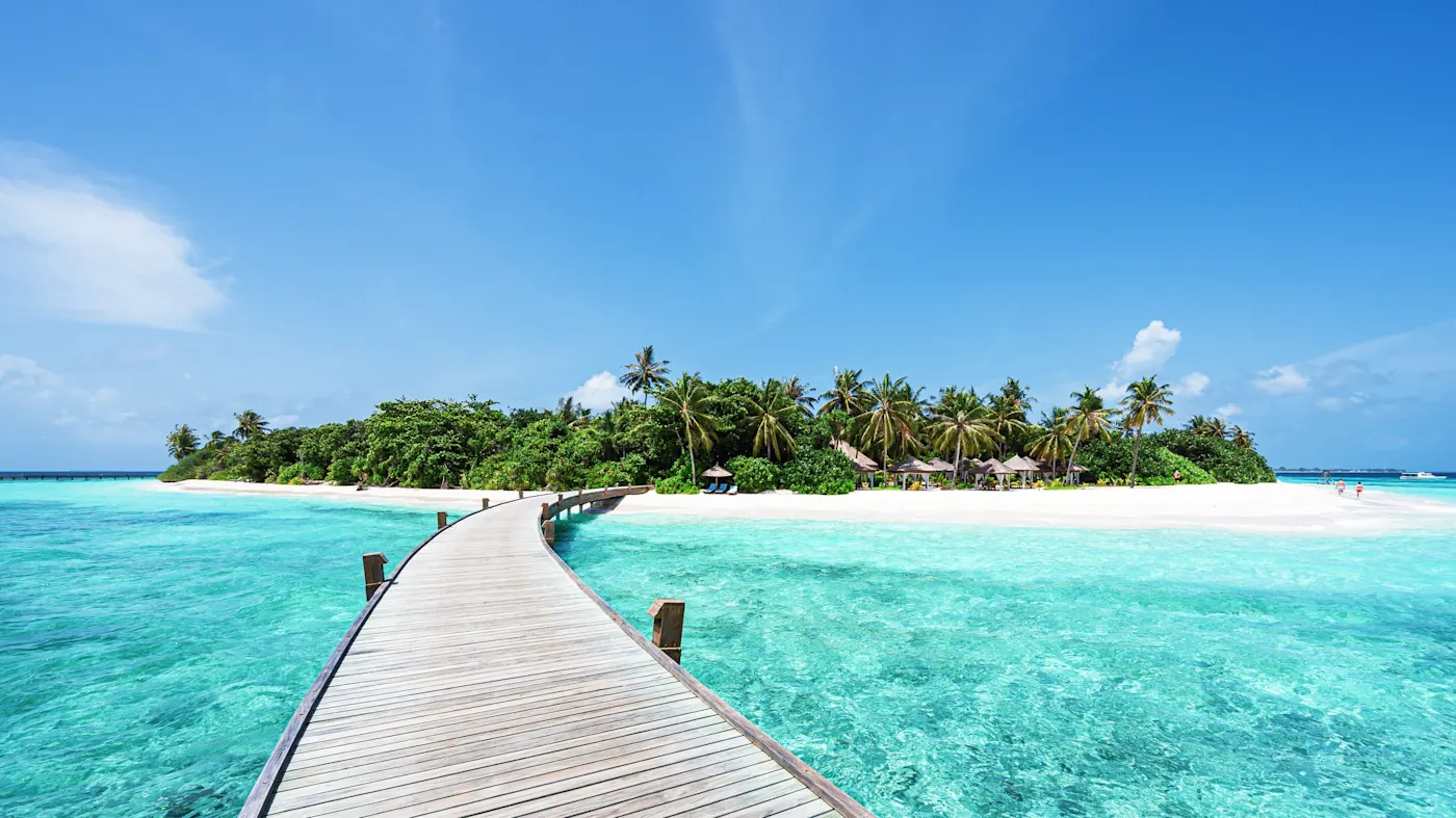 Raa Atoll, Malediven Holzsteg über türkisblaues Wasser zu einer tropischen Insel mit Palmen. Raa Atoll, Malediven.