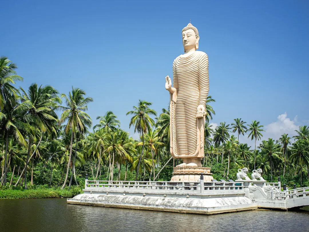 Große Buddha-Statue umgeben von Palmen an einem Wasserbecken. Hikkaduwa, Südprovinz, Sri Lanka.
