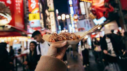 Japanisches Streetfood in einer mit Leuchtwerbung beschilderten Straße