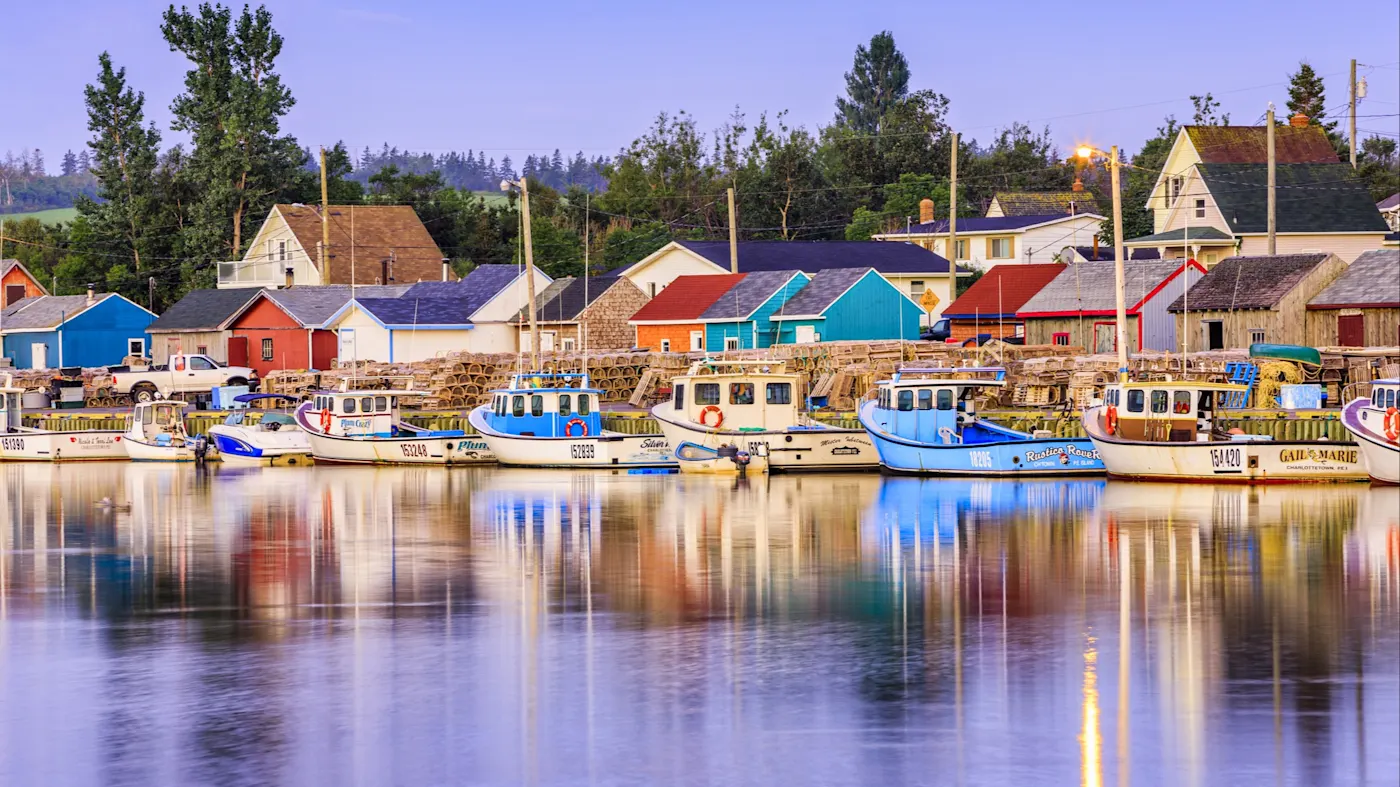 Prince Edward Island, Prince Edward Island, Kanada Fischerboote in einem Hafen mit bunten Häusern im Hintergrund bei ruhigem Wasser. Prince Edward Island, Prince Edward Island, Kanada.