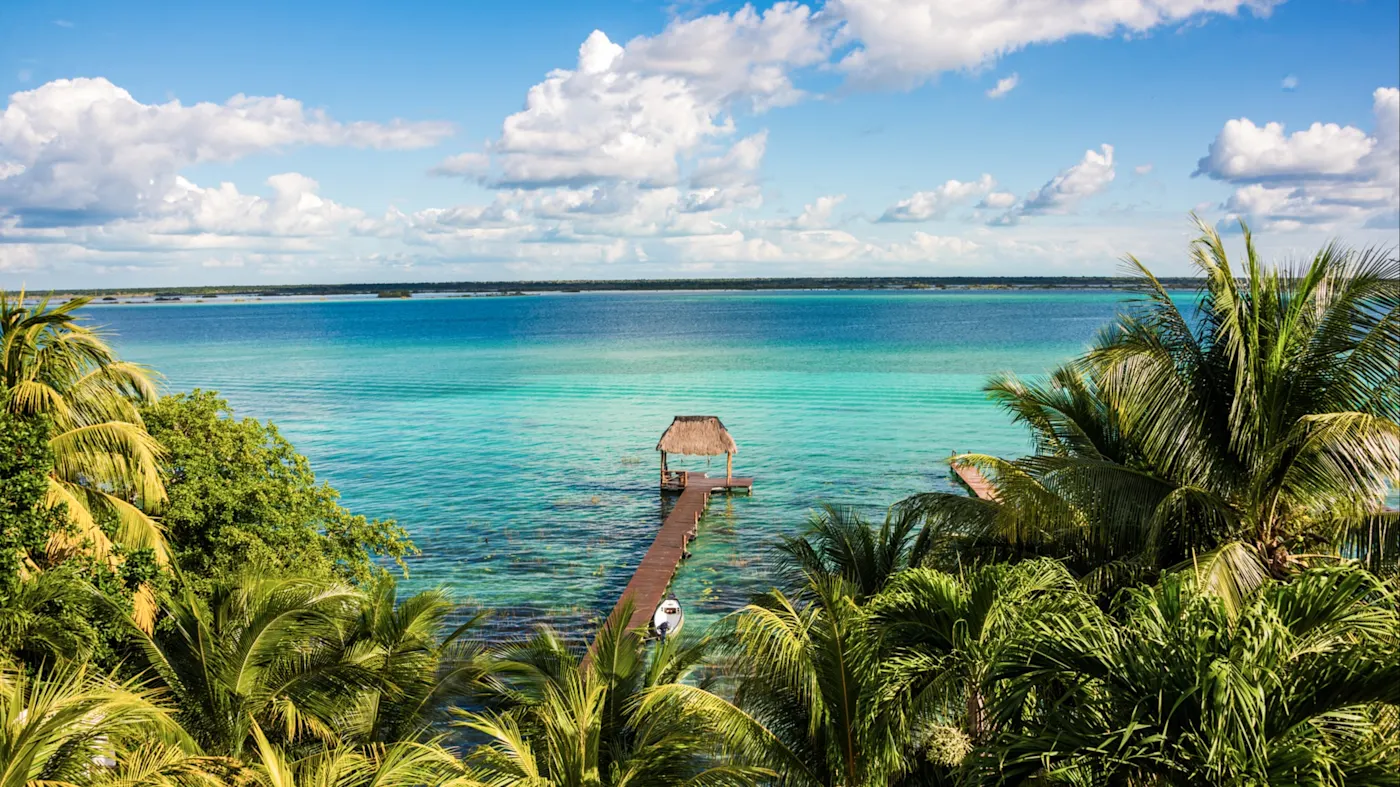 Panoramablick auf die smaragdgrüne Lagune und einen Steg mit Strohdach. Bacalar, Quintana Roo, Mexiko.
Alt tag Description French