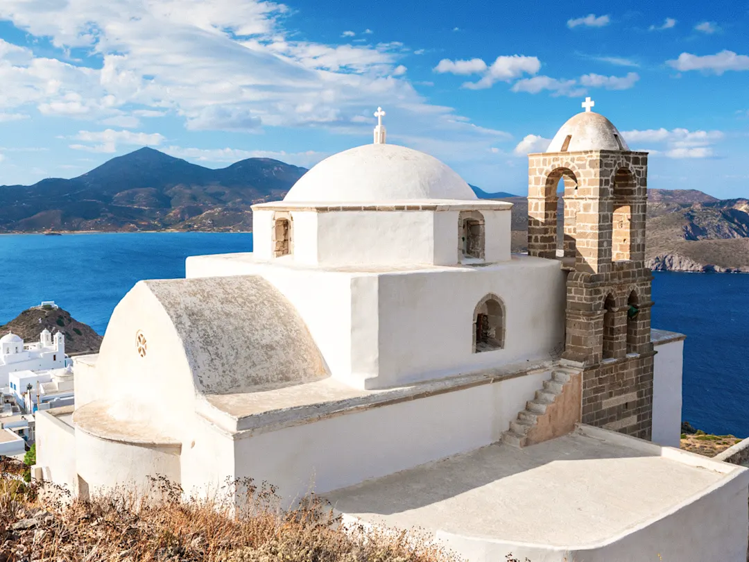 Traditionelle weiße Kirche mit Blick auf das Meer und umliegende Hügel, Plaka, Milos, Griechenland.