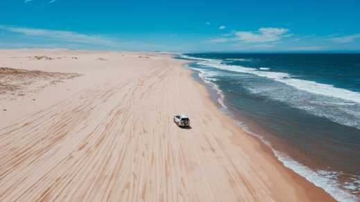 Magnifique vue aérienne sur un 4x4 en train de rouler sur une plage de sable rose pendant un voyage en Australie.