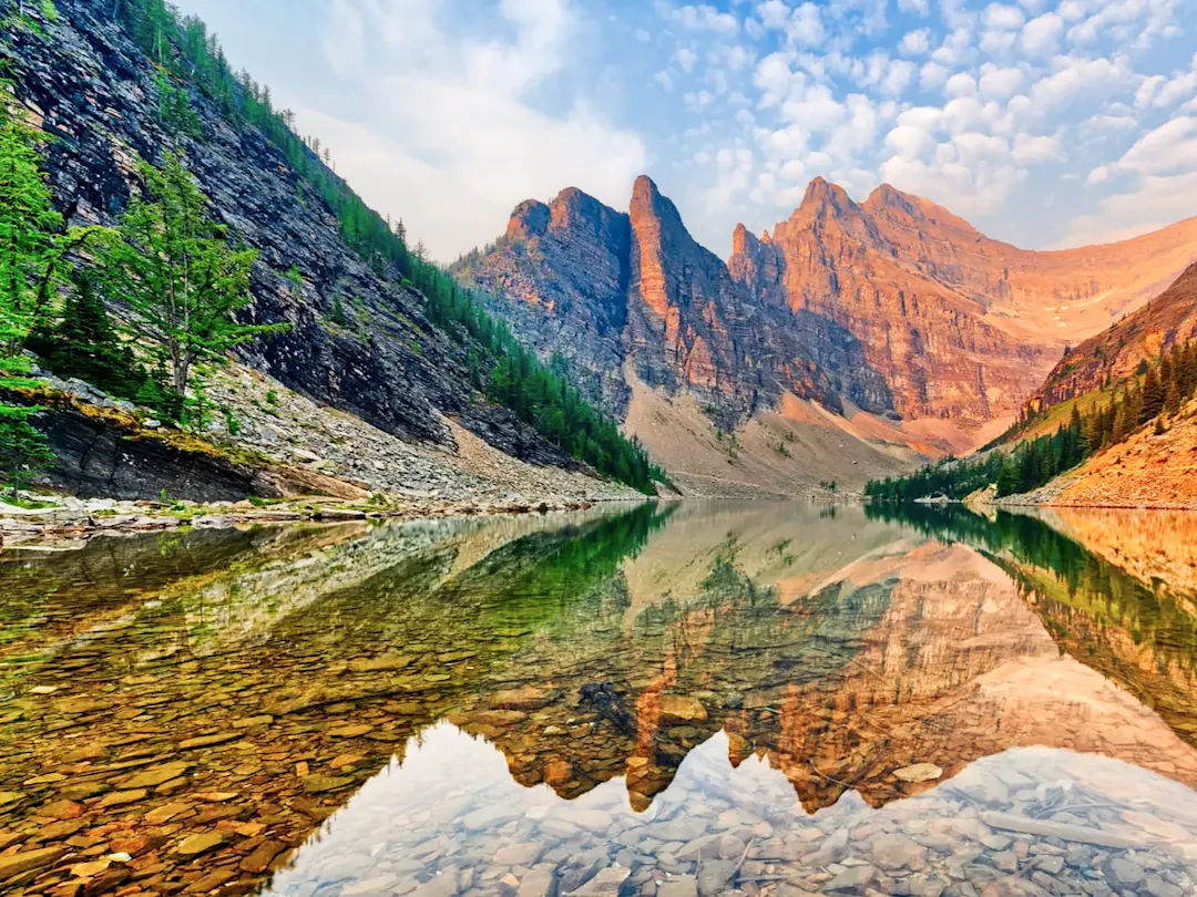 Kristallklarer Bergsee mit Spiegelung der Felsen bei Sonnenaufgang, Alberta, Kanada.