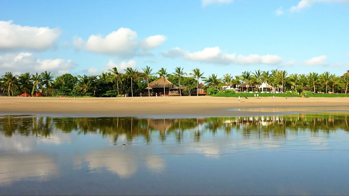 Seminyak, Bali, Indonesien Palmen und Strandhütten spiegeln sich im flachen Wasser am Sandstrand. Seminyak, Bali, Indonesien.
