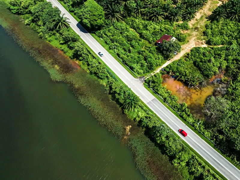 Malaysia, Roadtrip Straße neben einem Fluss, grüne Landschaft, rotes Dachhaus und zwei Autos. Malaysia.
