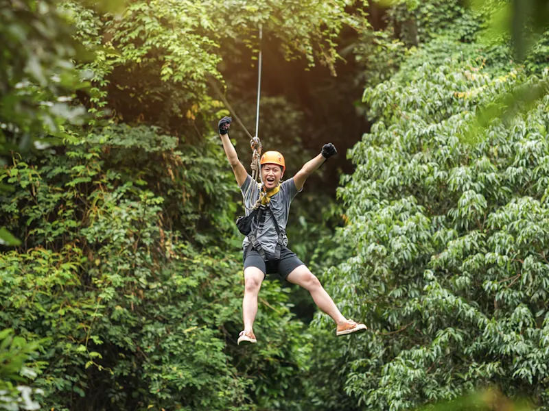 Mauritius, Ziplining, Mann Mann beim Ziplining durch üppigen Regenwald, lachend mit ausgestreckten Armen, Mauritius.