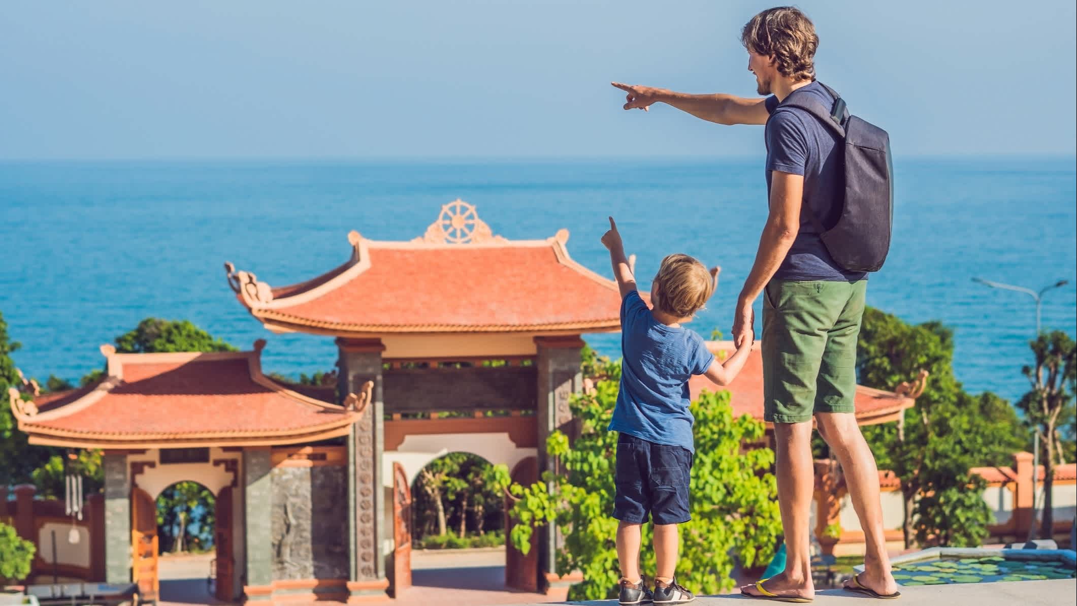 Un père et un fils montrant pointant le paysage du doigt devant un temple, à Phu Quoc, au Vietnam.