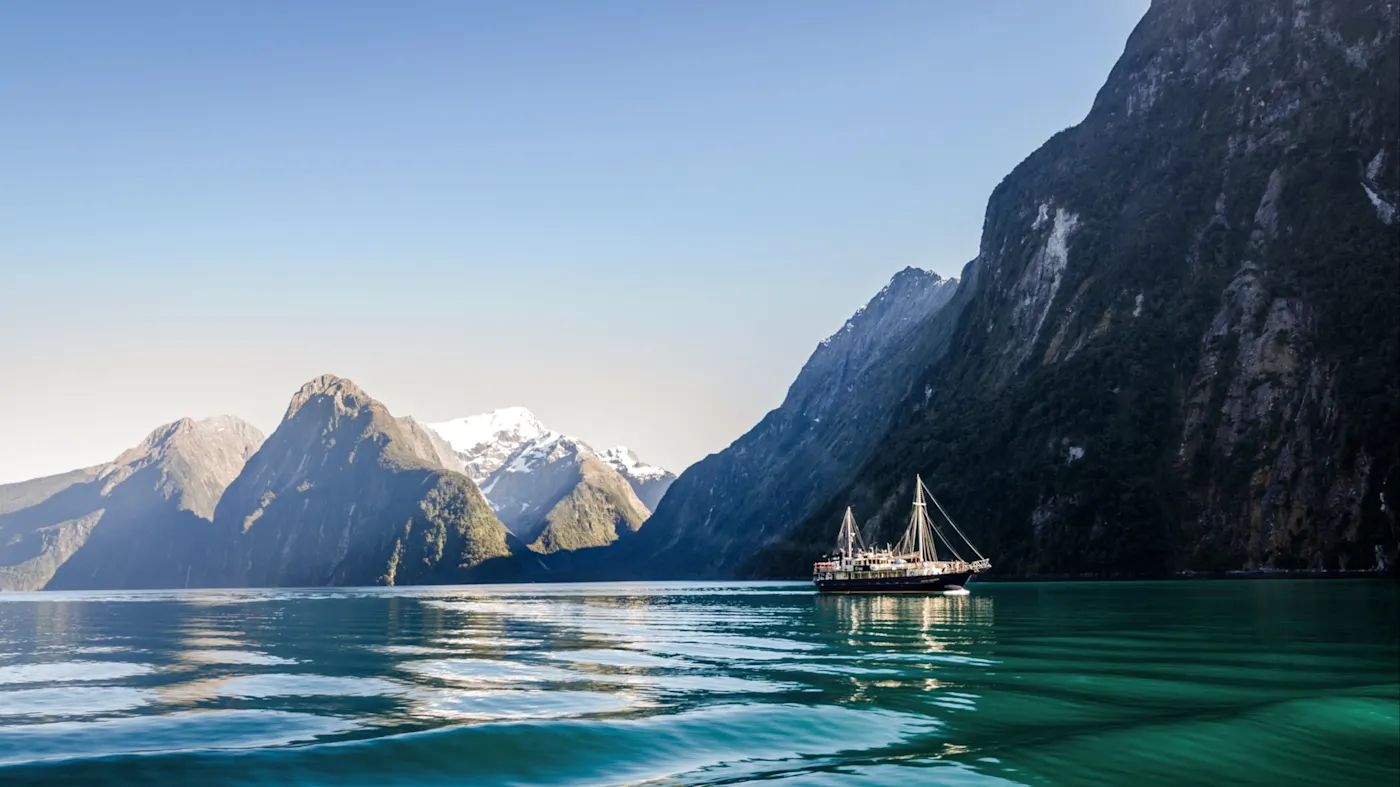 Milford Sound, Südinsel, Neuseeland Panoramablick auf Milford Sound mit Segelschiff, umgeben von majestätischen Bergen. Milford Sound, Südinsel, Neuseeland.