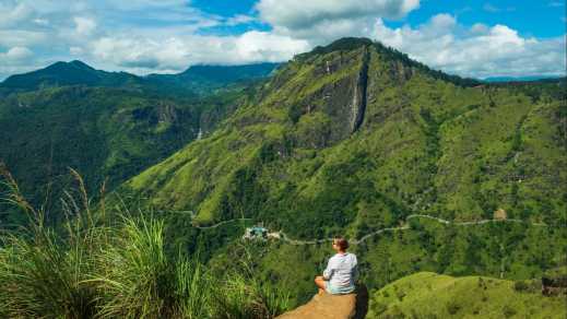 Frau sitzt auf Stein auf Little Adam's Peak mit Blick auf grüne Berge von Sri Lanka