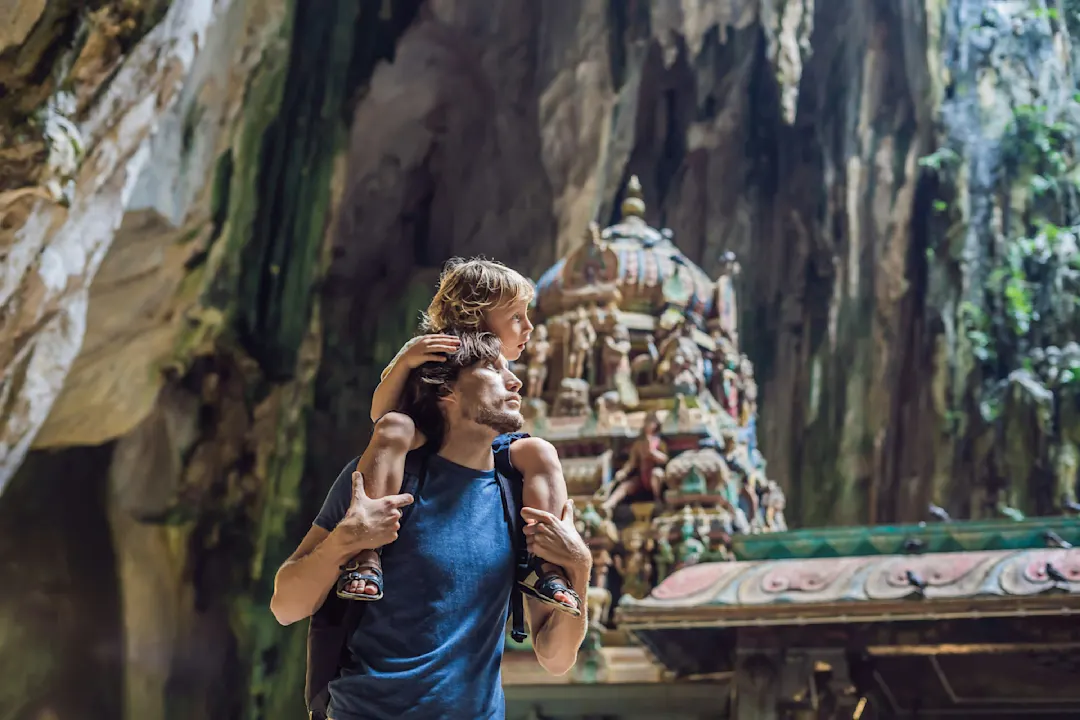 Kind auf den Schultern eines Erwachsenen in einer Höhle mit hinduistischem Schrein, umgeben von Felswänden.
