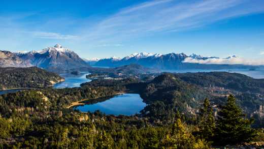 South America, Argentina, Bariloche, view from above of Nahuel Huapi Lake surrounded by forest and with snowy mountains in the background.