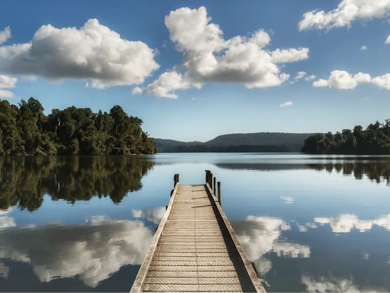 Lake Mapourika,, Südinsel, Neuseeland Steg aus Holz ragt in einen ruhigen See mit Spiegelung der Wolken, Lake Mapourika, West Coast, Neuseeland