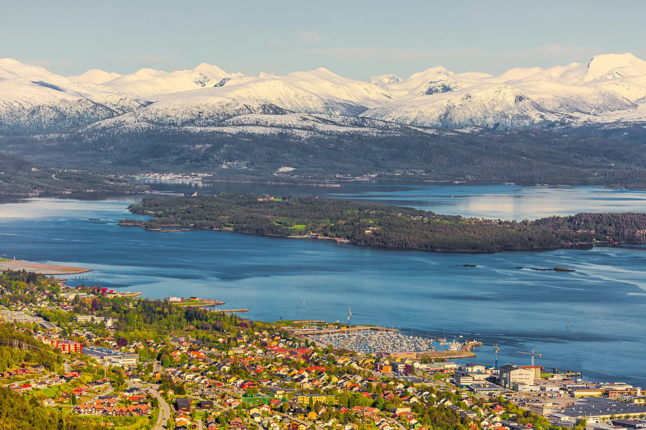 Am Fjord gelegene Stadt mit schneebedeckten Bergen im Hintergrund