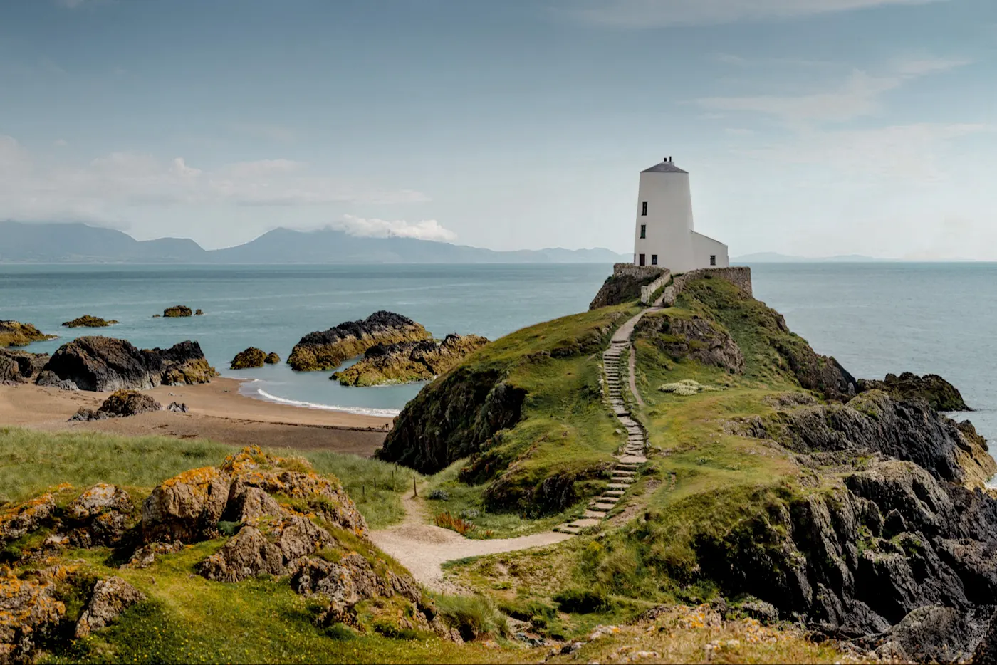 Weißer Leuchtturm, Steinstufen, grüner Hügel, Strand, Ozean, Holy Island, Wales.