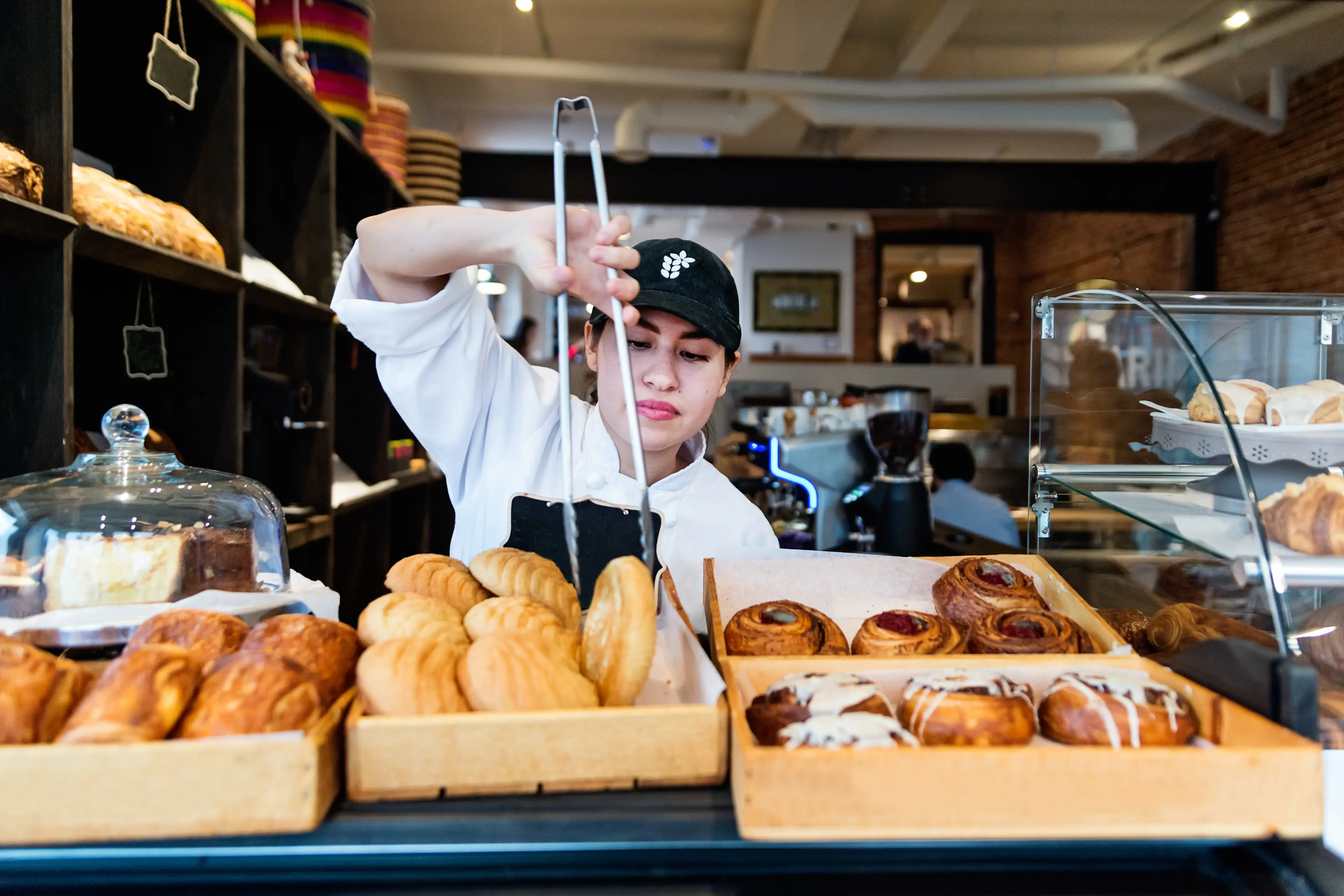 Stolzer Besitzer einer kleinen lokalen Bäckerei, die hinter der Theke ein Gebäck bekommt. Sie ist Mexikanerin, in ihren Dreißigern. Horizontale Taille nach innen Aufnahme mit Kopierraum. Dies wurde in Montreal, Kanada, aufgenommen.