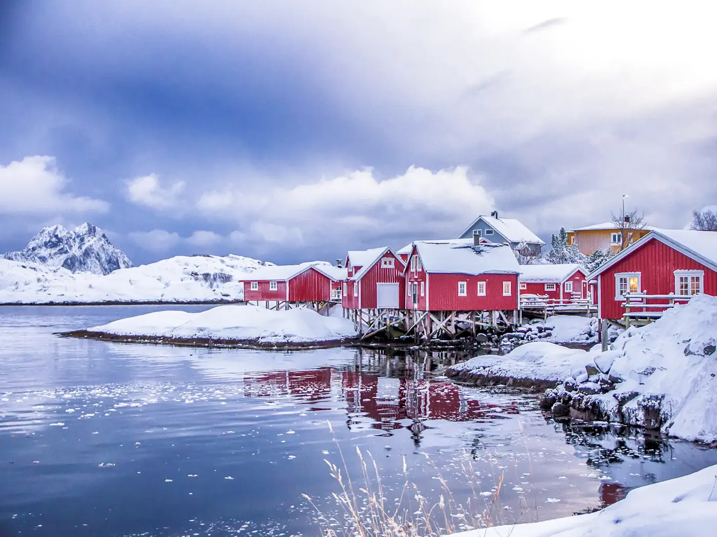 Rote Holzhäuser auf Stelzen am verschneiten Fjordufer. Lofoten, Nordland, Norwegen.