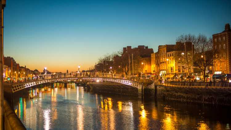 Discover Dublin's Ha'penny Bridge, here pictured at dusk with lights reflected in the water, on a Dublin vacation