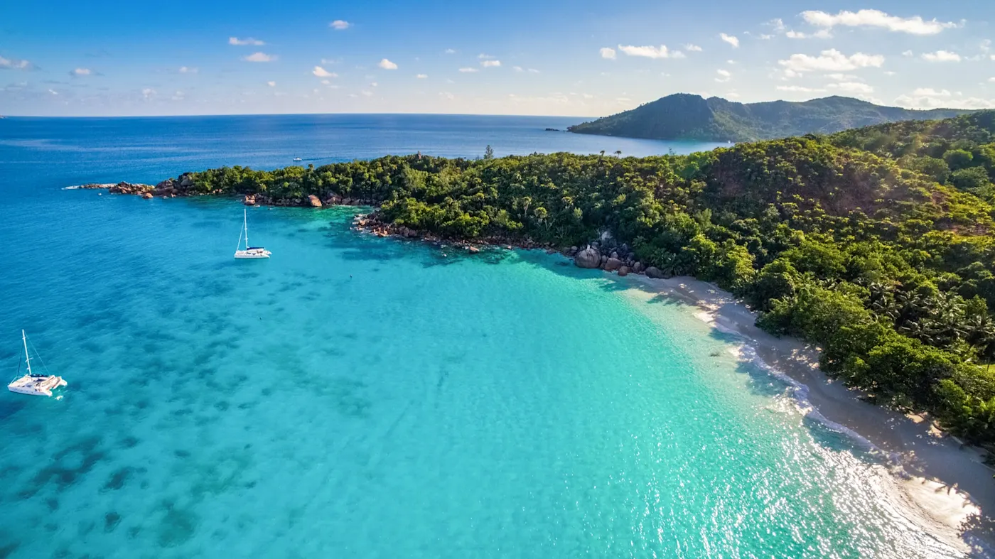 Praslin, Seychellen Türkisblaue Bucht mit Sandstrand und Segelbooten, umgeben von tropischer Natur. Praslin, Seychellen.