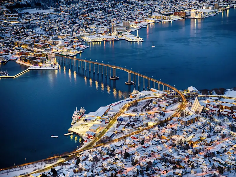 Nachtpanorama mit beleuchteter Brücke und verschneiter Stadt. Tromsø, Troms, Norwegen.