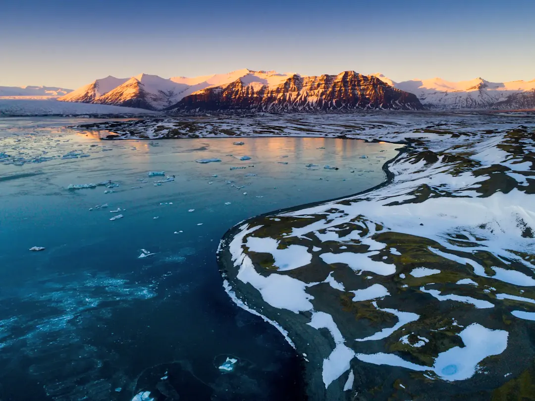 Gletschersee mit treibenden Eisschollen und Bergen im Sonnenuntergang. Island