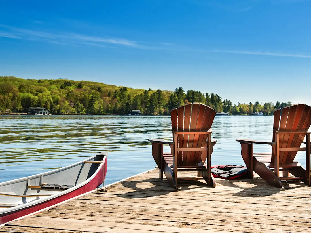 Zwei Holzstühle auf einem Steg mit Kanu am ruhigen See. Muskoka, Ontario, Kanada.
