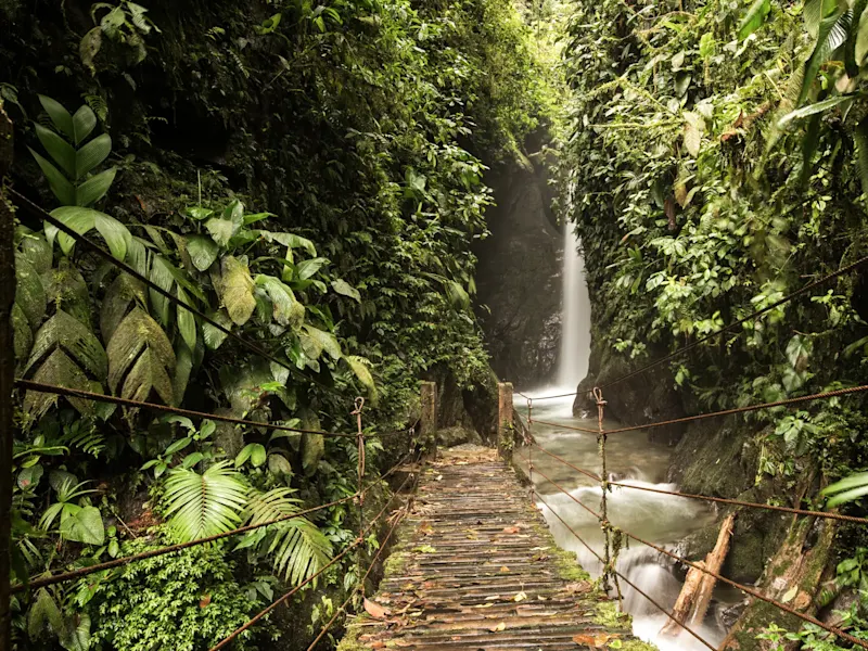 Ecuador, Napo, Tena Hängebrücke im Dschungel mit Wasserfall in einer Schlucht. Tena, Napo, Ecuador.