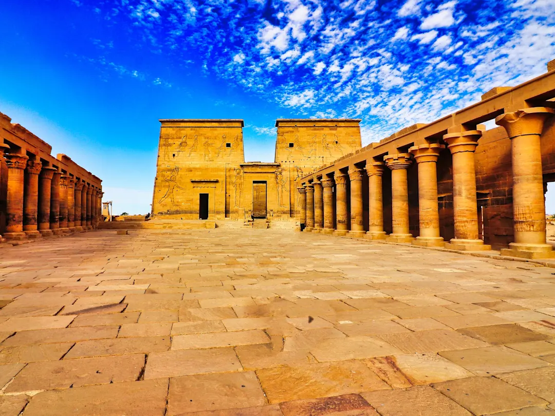 Assuan, Ägypten Der Philae-Tempel mit beeindruckenden Säulen und Reliefs, umgeben von Wasser, unter blauem Himmel mit weißen Wolken, in Assuan, Ägypten.