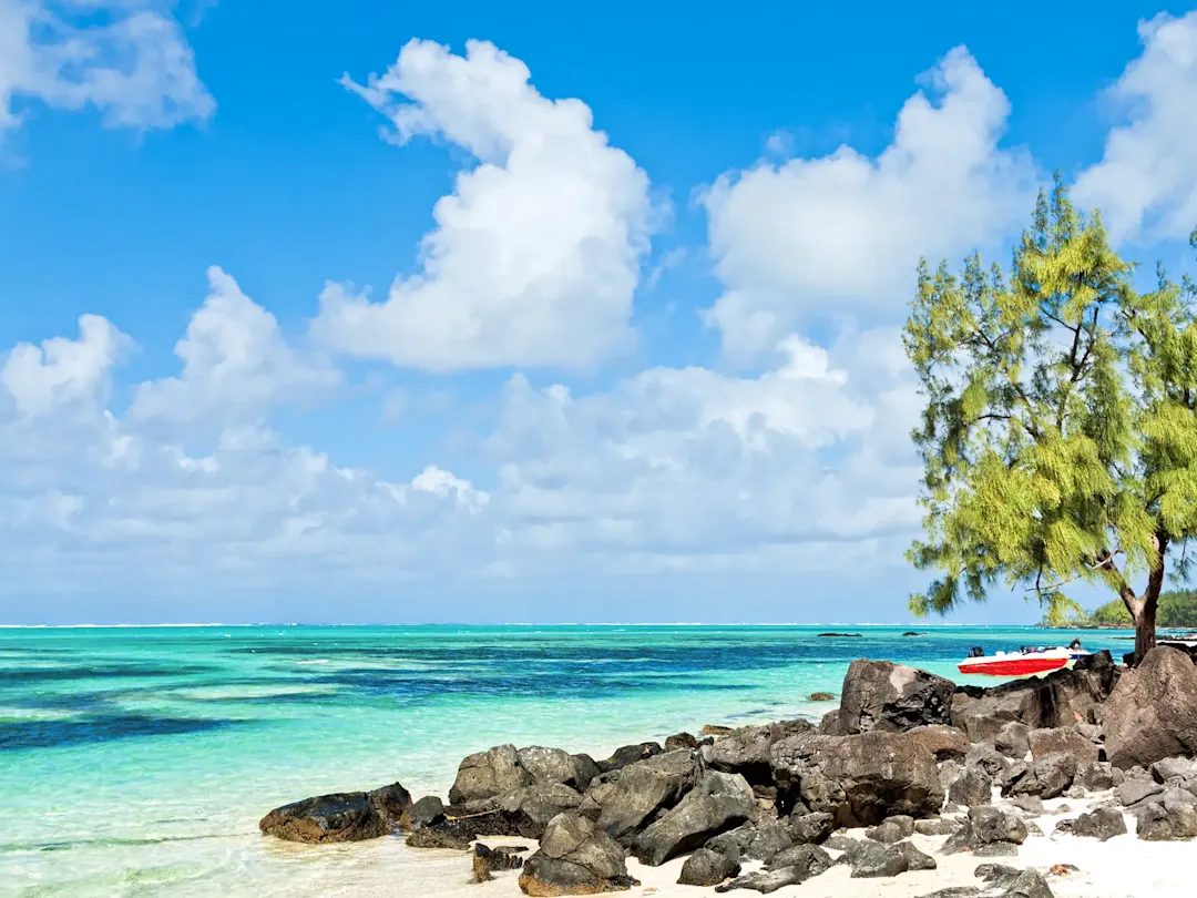 Idyllischer Strand mit türkisfarbenem Wasser, Felsen und Boot unter blauem Himmel. Mauritius.