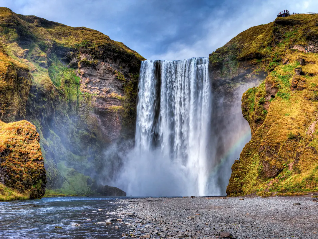 Mächtiger Wasserfall mit grünen Klippen und Regenbogen. Skógafoss, Südisland, Island.