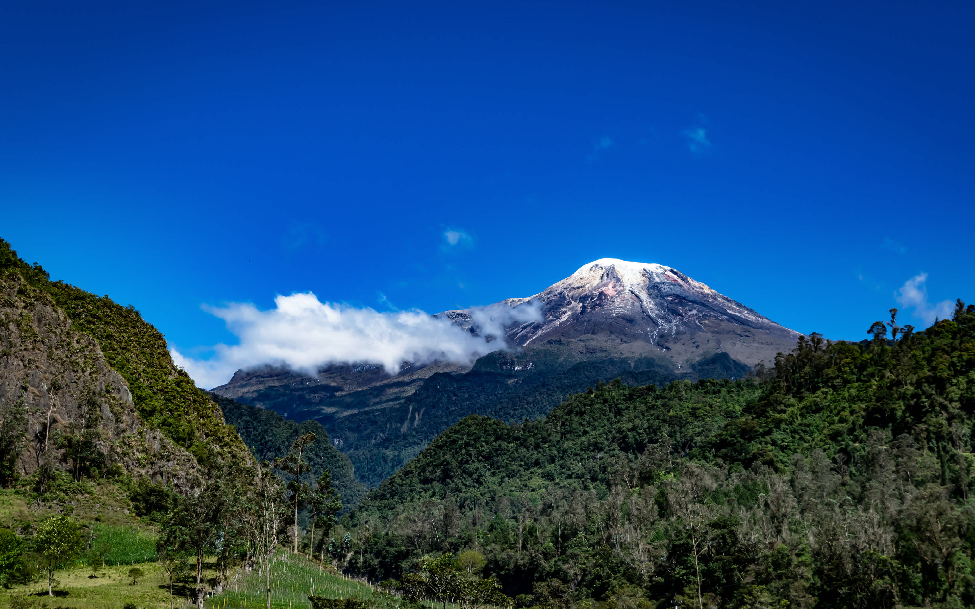 Schöner Blick auf den schneebedeckten Gipfel des Tolima vor einem strahlend blauen Himmel mit wenigen Wolken, aufgenommen vom Stadtrand von Ibague Tolima