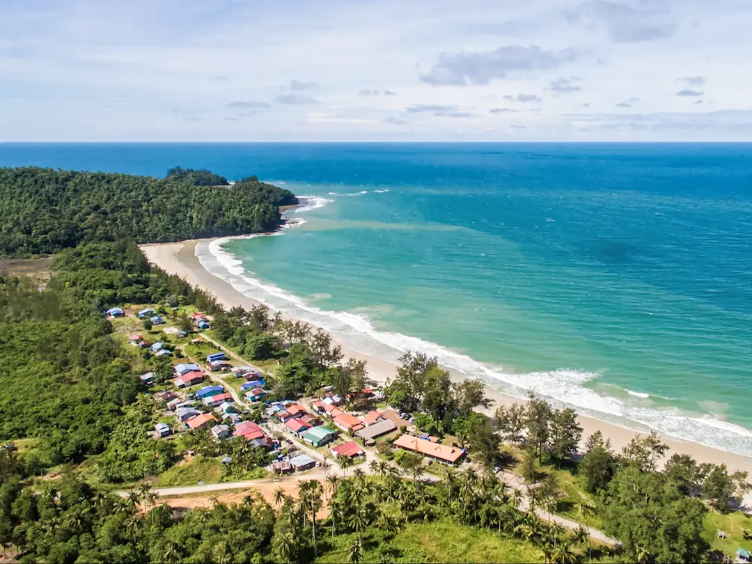 Tropisches Dorf an einer grünen Küste mit türkisfarbenem Meer. Kampung Mengkabong, Sabah, Malaysia.