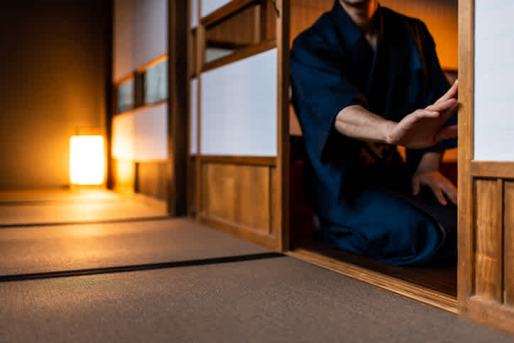 Un homme en kimono ouvre la porte coulissante en bois et papier de sa chambre dans un ryokan, une auberge traditionnelle japonaise. Une expérience à vivre pendant votre voyage au Japon !