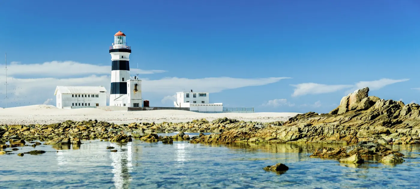 Port Elizabeth, Ostkap, Südafrika Schwarz-weißer Leuchtturm an einem felsigen Strand mit klarem Wasser. Port Elizabeth, Ostkap, Südafrika.