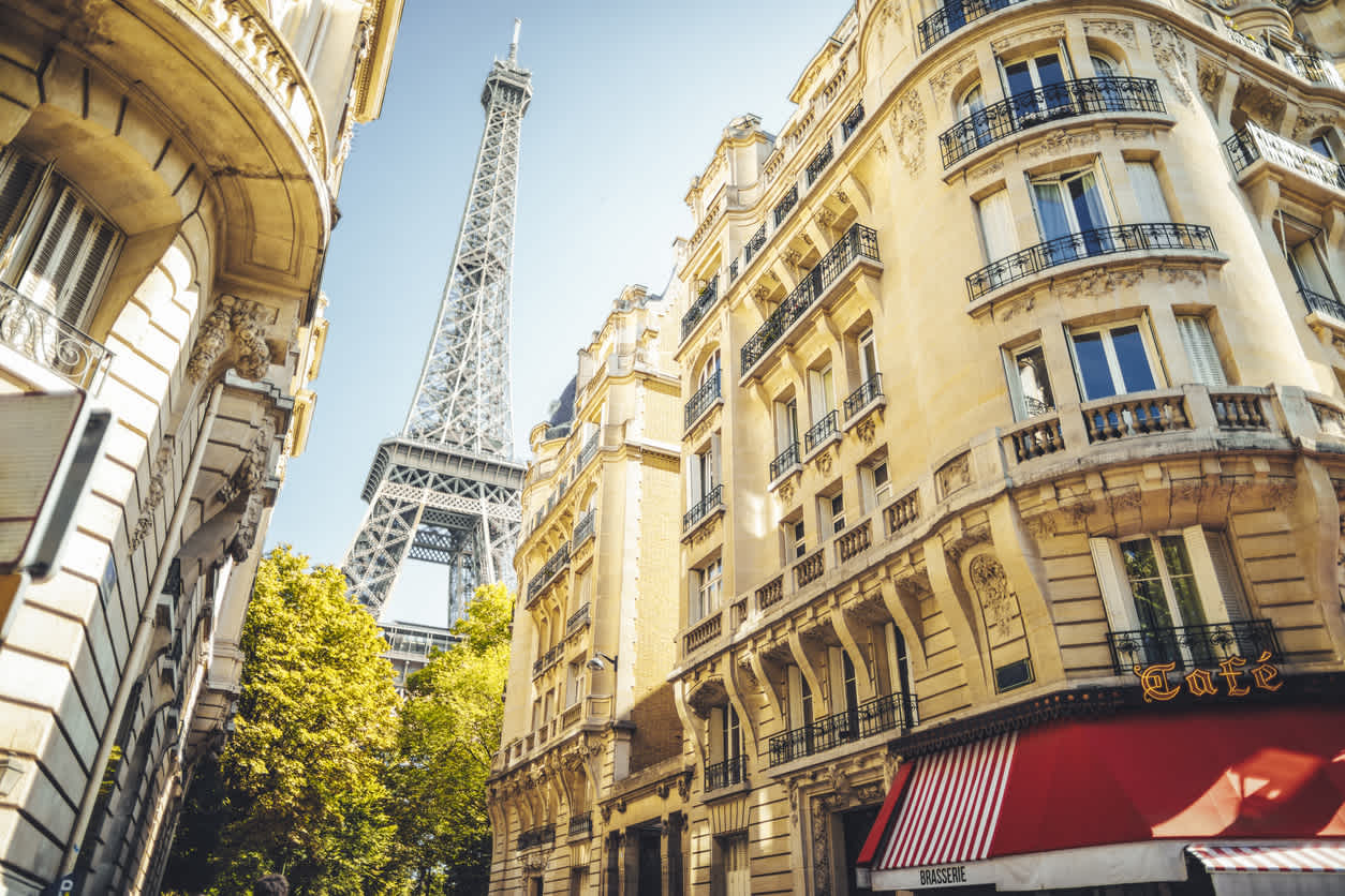 Une rue parisienne avec des immeubles de style Haussmannien par une journée ensoleillée et la Tour Eiffel en arrière-plan.