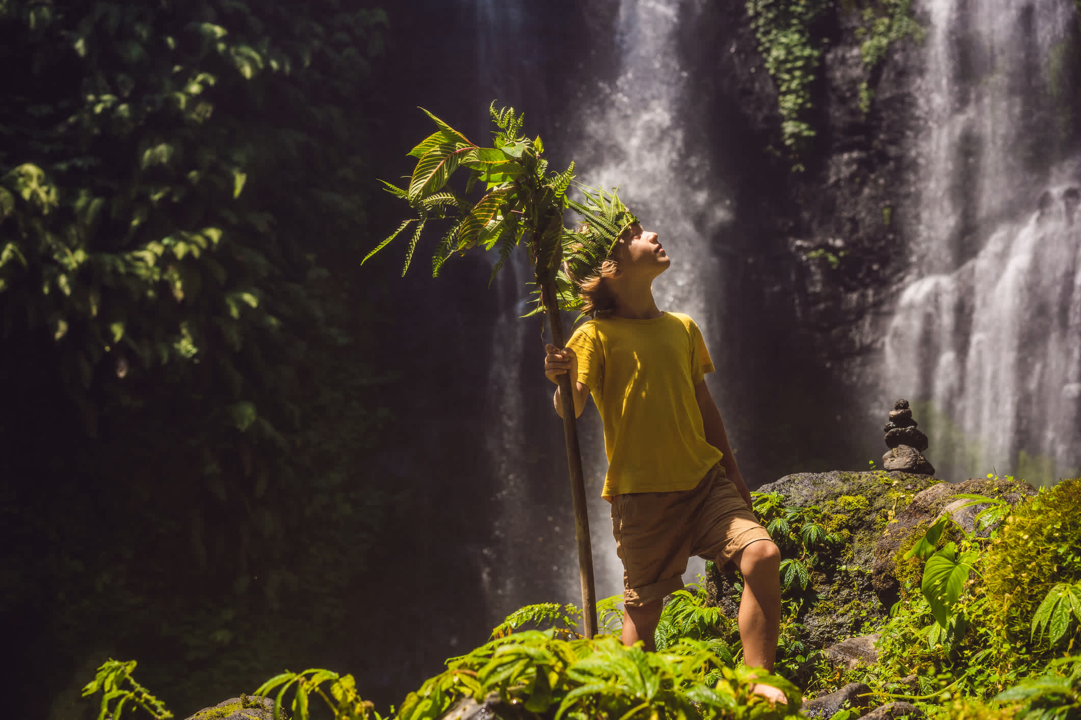 Un garçon dans la jungle avec une chute d'eau en toile de fond.