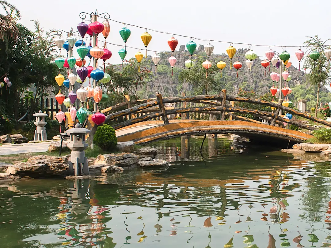 Bunte Laternen und Brücke über einen Teich im Garten. Ninh Binh, Vietnam.
