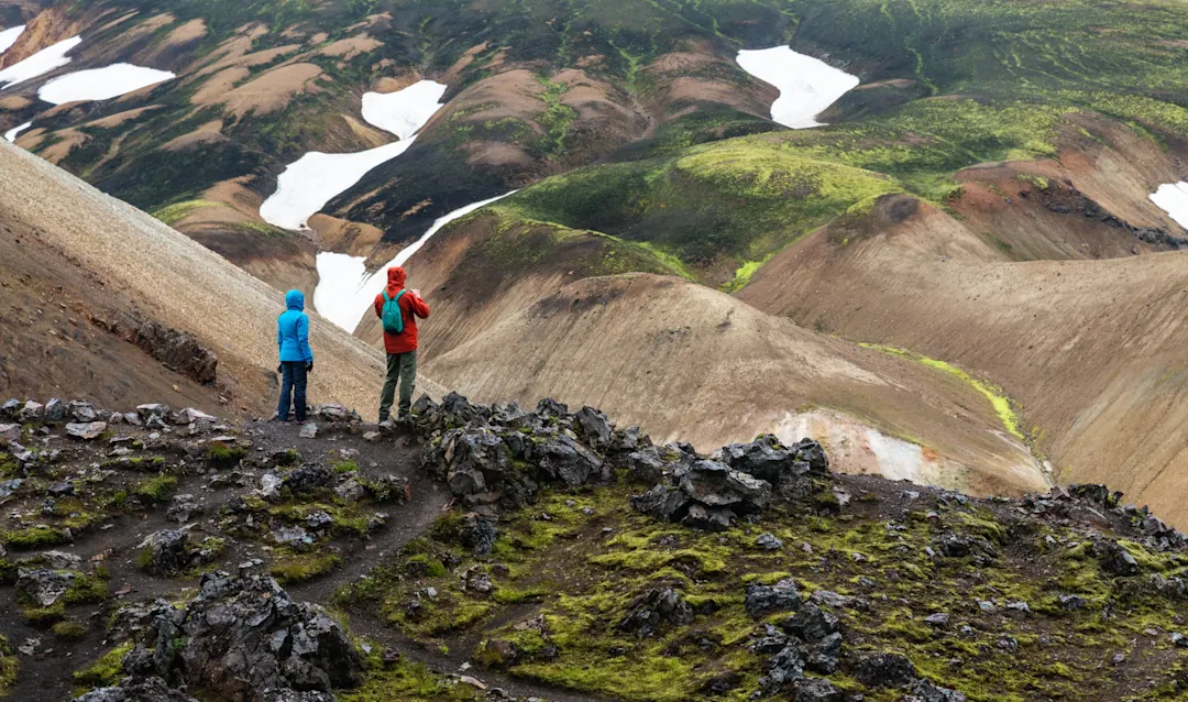 Wanderer in bunter Rhyolith-Berglandschaft mit Schneefeldern, Landmannalaugar, Suðurland, Island.