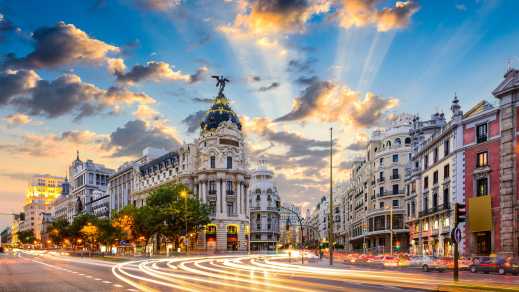Europe, Spain, Madrid, a busy street corner in Madrid. Traffic streaks by, and the late afternoon sun lights up a blue sky dotted with clouds.